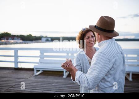 Glückliches Seniorenpaar, das auf dem Pier am Meer tanzt und sich anschaut. Stockfoto