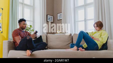 Junges gemischtes Paar süchtig nach Smartphones, die zu Hause auf dem Sofa sitzen. Stockfoto