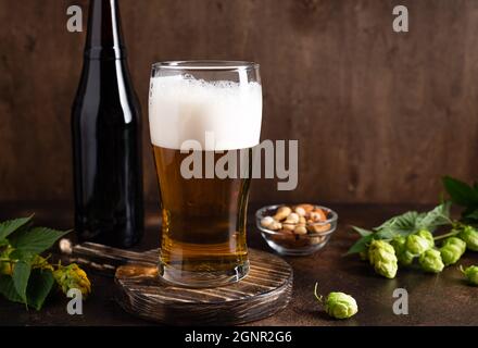 Kaltes Bierglas mit Schaum, Snacks und Bierflasche auf dunklem Holzhintergrund Stockfoto
