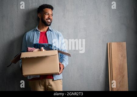 Glücklicher junger Mann, der Packkisten hält, nach Hause zieht, Platz kopiert. Neues Wohnkonzept. Stockfoto