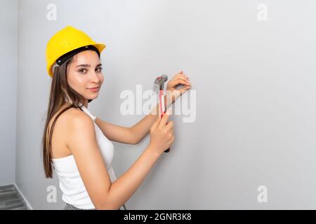 Eine junge Arbeiterin trifft den Hammer, um sich für den Bau oder die Renovierung an die Wand zu nageln. Hochwertige Fotos Stockfoto