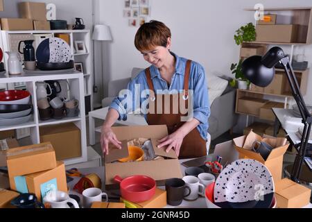 Reife asiatische Frau Unternehmer, Unternehmer Verpackung keramische Produkte in Verpackungen für Lieferung und Versand. Online-Verkauf Geschäft Arbeit bei hom Stockfoto