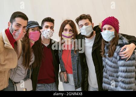 Freunde mit Gesichtsmasken, die Spaß daran haben, die Hände auf den Schultern zu umarmen Stockfoto