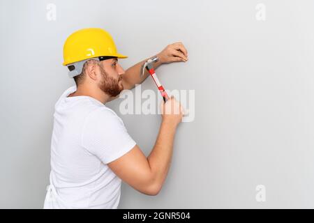 Ein junger Arbeiter trifft den Hammer, um ihn für Bauarbeiten oder Renovierungen an die Wand zu nageln. Hochwertige Fotos Stockfoto