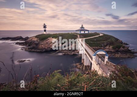 Schöner Blick auf den Leuchtturm Faro Illa Pancha mit einer Brücke unter wolkenfreiem Himmel in Galicien, Spanien Stockfoto