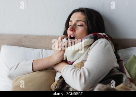 Kranke Frau, die mit geschlossenen Augen im Bett liegt, mit Rachenspray Stockfoto