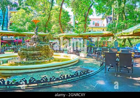 Der malerische Brunnen und das Restaurant im Freien im schattigen und grünen Palais Royal Park im alten Odessa, Ukraine Stockfoto
