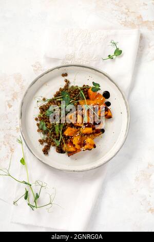 Salat mit gebackenem Kürbis, Linsen und Balsamico-Dressing, garniert mit Erbsen-Microgreens auf hellem Hintergrund. Gesundes veganes Essen, Draufsicht Stockfoto