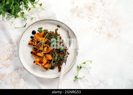 Salat mit gebackenem Kürbis, Linsen und Balsamico-Dressing, garniert mit Erbsen-Microgreens auf hellem Hintergrund. Gesundes veganes Essen, Draufsicht Stockfoto