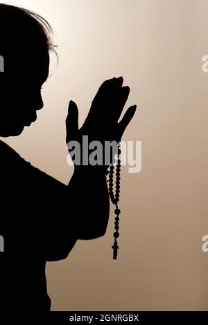 Silhouette einer treuen Frau, die bei Sonnenuntergang mit Rosenkranz betet. Konzept für Religion, Glauben, Gebet und Spiritualität. Stockfoto