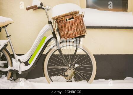 Holländisches Fahrrad mit Korb bedeckt mit Schnee während der Winterzeit vor einem alten Haus geparkt Stockfoto