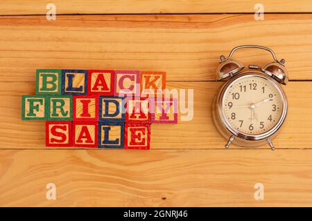 SPEKTAKULÄRES KONZEPT VON SCHWARZEM FREITAG UND VERKAUF MIT HOLZWÜRFELN UND HOLZOBERFLÄCHE MIT ALTEM WECKER. Stockfoto