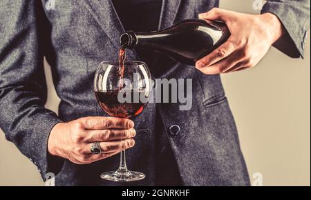 Rotwein wird von Flasche zu Glas gegossen. Gourmet-Getränkeflasche, Rotweinglas, Sommelier, Verkostung. Kellner gießt Rotwein in ein Glas. Sommelier Stockfoto
