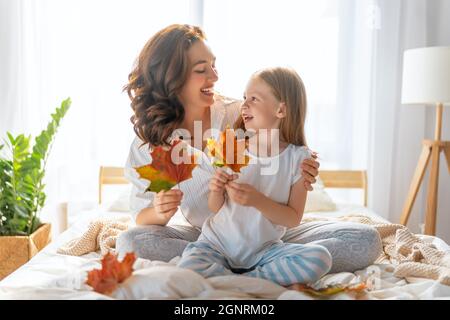 Ein nettes Mädchen und ihre Mutter genießen sonnigen Morgen. Gute Zeit zu Hause. Kind wacht aus dem Schlaf auf. Familie spielt auf dem Bett im Schlafzimmer. Stockfoto