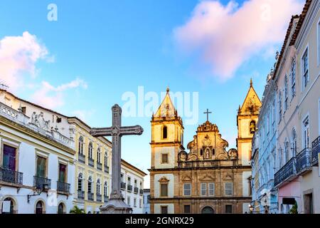 Alte Häuser und Kirchen im kolonialen und barocken Stil mit einem Kruzifix auf dem zentralen Platz des historischen Pelourinhoviertels in Salvador, Bahia Stockfoto