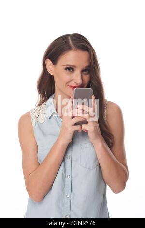 Portrait of content hübsche junge Frau in ärmellosem Hemd hält Gadget in der Nähe des Gesichts, isolierten Hintergrund Stockfoto