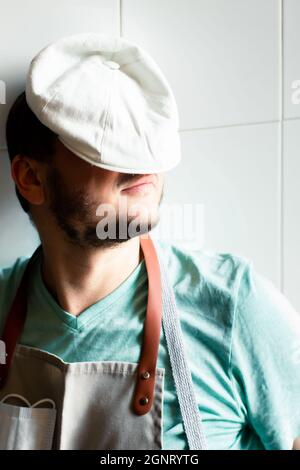 Ein junger Bäcker in einer Mütze und Schürze schläft auf einer Arbeit in einer Bäckerei. Ermüdungskonzept. Stockfoto