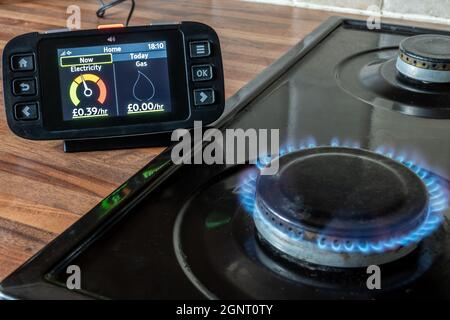 Intelligentes Messgerät zur Messung des Gas- und Stromverbrauchs auf einem intelligenten Energiemonitor neben einem Herd mit Gaskochflamme Stockfoto