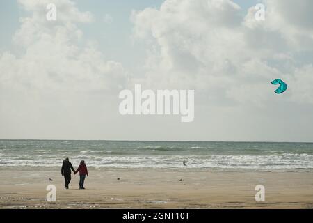 Gower, Swansea, Großbritannien. September 2021. UK Wetter: Ein windiger Herbsttag mit Sonnenschein und Schauern am Llangennith Beach auf der Gower Halbinsel. Ein Windsurfer nutzt die steife Brise an Land, wenn ein angemessen gekleidetes Paar am Strand spazieren geht. Kredit: Gareth Llewelyn/Alamy Stockfoto