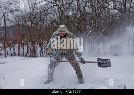 Mit Shovel räumt der Mann den Hof vom Schnee. Starker Schneefall im Winter. Hoher Schneestand. Schneeverwehung. Stockfoto