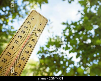 Holzthermometer mit roter Messflüssigkeit, die an sonnigen Tagen im Schatten der Bäume eine hohe Temperatur von über 34 Grad Celsius zeigt. Konzept der Hitzewelle, w Stockfoto