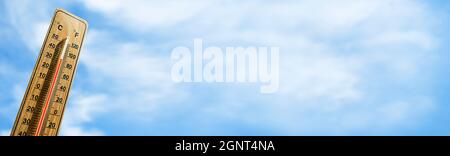 Holzthermometer mit roter Messflüssigkeit, die eine hohe Temperatur von über 32 Grad Celsius auf dem Hintergrund des blauen Himmels zeigt. Panorama. Konzept der Wärme wav Stockfoto