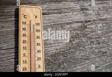 Holzthermometer mit roter Messflüssigkeit, die am sonnigen Tag auf altem Holzhintergrund eine hohe Temperatur von über 32 Grad Celsius anzeigt. Konzept der Wärme w Stockfoto