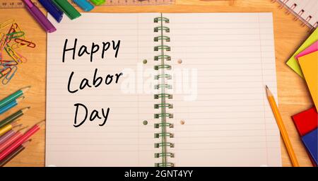 Happy Labor Day Text über offenes Buch gegen mehrere Schulausrüstung auf Holztisch Stockfoto