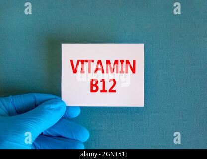 Vitamin B12-Symbol. Weiße Note mit den Worten Vitamin B12, schöner blauer Hintergrund, Arzthand in blauem Handschuh. Medizinisch, Vitamin B12 Konzept. Stockfoto