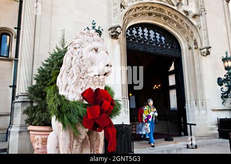 Eine mit einem Weihnachtsbogen geschmückte Statue eines Schutzlöwens am Eingang des Biltmore Estate, das im Herbst in Asheville, North Carolina, im Privatbesitz der Familie Vanderbilt ist. Das Haus ist das größte Privathaus in Amerika mit über 250 Zimmern. Stockfoto