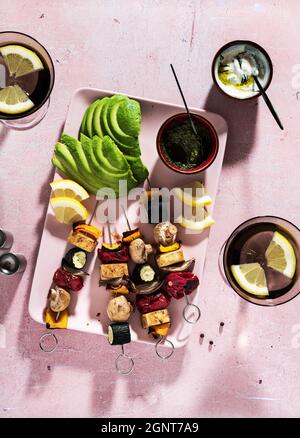 Geröstete Veggie-Kebabs mit Tofu und Pilzen, Avocado und Basilikum-Pesto. Tzatziki-Sauce und Sommercocktail auf einem rosafarbenen Tisch Stockfoto