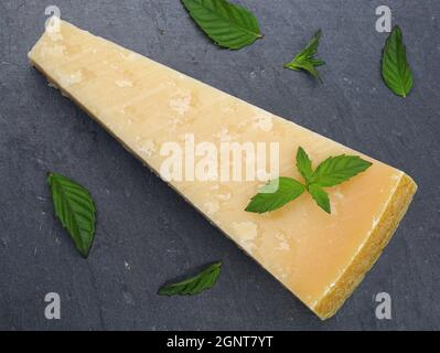 Draufsicht auf Parmigiano reggiano oder Parmesan auf dunklem Schieferteller mit grünen Minzblättern Stockfoto