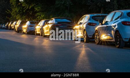 Gelb-orange Sonne Sterne während des Sonnenuntergangs auf einer langen Reihe von geparkten Autos im Stadtpark am Abend. Reihe von Autos Stockfoto