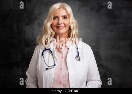 Studioportrait einer älteren Ärztin, die auf einem isolierten dunklen Hintergrund liegt. Speicherplatz kopieren. Stockfoto