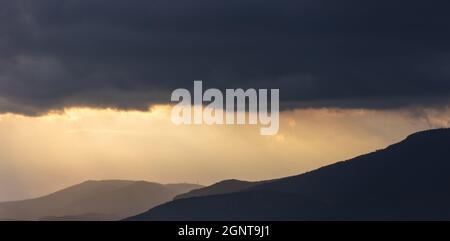 Dunkelgraue Wolken am dramatischen Himmel bei Sonnenuntergang Hintergrund, Raum. Schwere Wolkenlandschaft über Bergen. Schlechtes Wetter, Regen und Gewitter. Stürmisch regnerische Natura Stockfoto