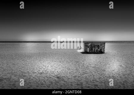 Monochrom-Bild von isolierten Paar am Strand, Great Yarmouth, Großbritannien. Mit Strand und Meer mit Graffiti Gebäude. Stockfoto