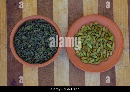 Tonschüssel voller grüner Kardamome und eine weitere Schüssel voller grüner Teeblätter auf Musterhintergrund gelegt Stockfoto