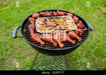 Hühnerschenkel unter Grillsauce und Kartoffelscheiben, die auf einem Holzkohlegrill gebacken und geräuchert wurden Stockfoto