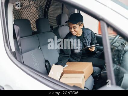 Lächelnde Frau, die auf dem Fahrersitz sitzt und Pakete überprüft und ein digitales Tablet in der Hand hält Stockfoto