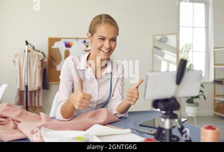 Glückliche Näherin Frau zeigt Daumen nach oben während der Meisterklasse für ihr Online-Publikum. Stockfoto