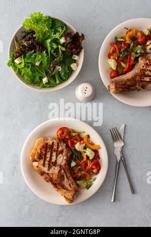 Köstliches herzhaftes Abendessen auf Tellern auf dem Tisch, gebratenes Schweinefleisch-Entrecote auf dem Knochen mit geschmortem Gemüse und frischem Salat mit Mozzarella Stockfoto