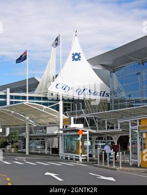 Die Abflugebene am internationalen Flughafen von Auckland in Auckland, Neuseeland, zeigt den Namen City of Sails vor seinem Haupteingang an. Die Abflugebene Straße vor dem Flughafeneingang wird von Reisenden genutzt, die an einem sonnigen Tag im November 2004 mit Gepäck reisen. Die neuseeländische Flagge schwingt über dem Terminaleingang. Stockfoto