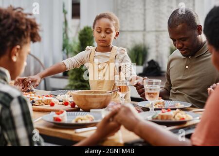 Porträt einer afroamerikanischen Familie, die beim Abendessen im Freien die Hände hält und betet, Platz zum Kopieren Stockfoto