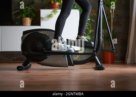 Beine einer Frau, die auf einem elliptischen Fahrrad im Wohnzimmer zu Hause trainiert Stockfoto