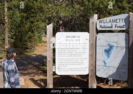 Ein Mann, der auf ein Schild am Eingang zum Waldo Lake in der Nähe von Oakridge, Oregon, in den Cascade Mountains schaut. Stockfoto