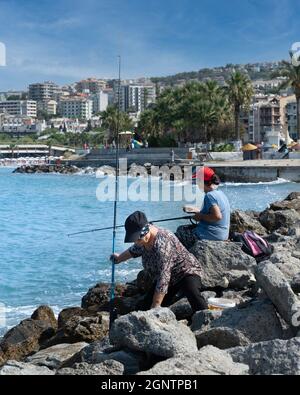 Kusadasi, Aydin, Türkei - 23. August 2021: Zwei Frauen sitzen auf Felsen am Meer und fischen. Stockfoto