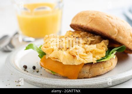 Englisches Muffin mit Rührei und Käse zum Frühstück, serviert mit einem Glas Orangensaft Stockfoto