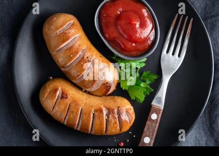 Gegrillte Würstchen und Ketchup auf schwarzem Teller, Draufsicht Stockfoto