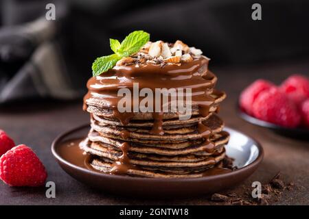 Schokoladen-Pfannkuchen mit Schokoladensirup, Nüssen und Himbeeren. Süße Schokoladenpfannkuchen zum Frühstück Stockfoto