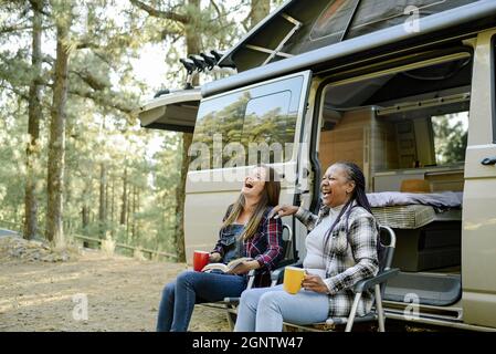 Multirassische Reisende Frauen, die in der Nähe des Campers lachen Stockfoto